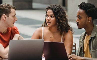 Three students collaborate over laptops