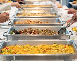 Photo displaying a line of silver buffet containers with prepared food