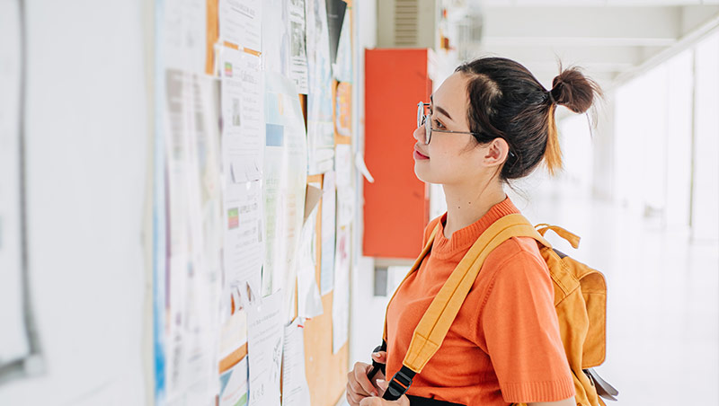 A student wearing a backpack looks at a bulletin board