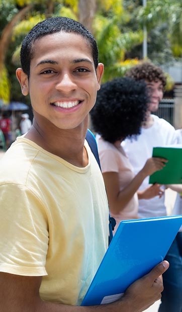 International student holds a folder and smiles at camera while fellow students stand in the background