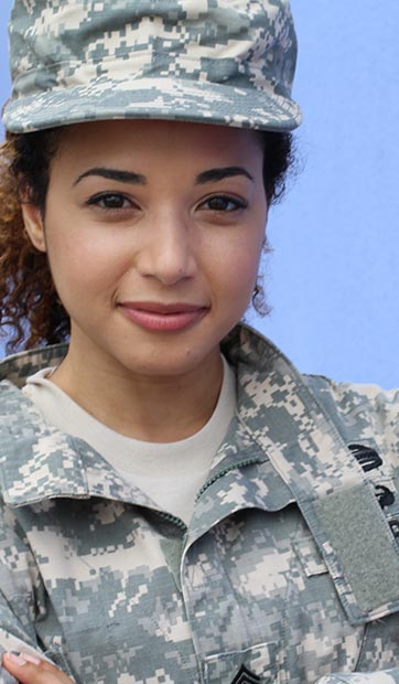 A Veteran woman in fatigues smiles at the camera with crossed arms
