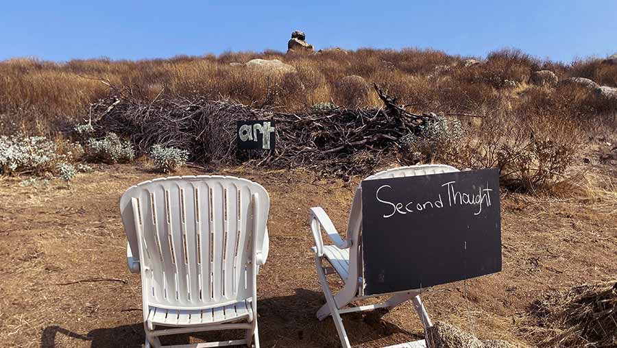 Making Refuge installation showing two plastic lawn chairs staring at a pile of wood with a sign labeled ART in front