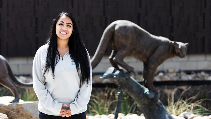 Arlene Serrato poses in front of bronze statues of mountain lion mascots by the Welcome Center building