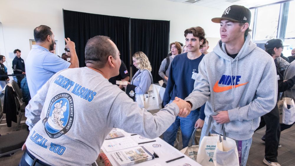 A student attendee accepts a handshake from a trade worker