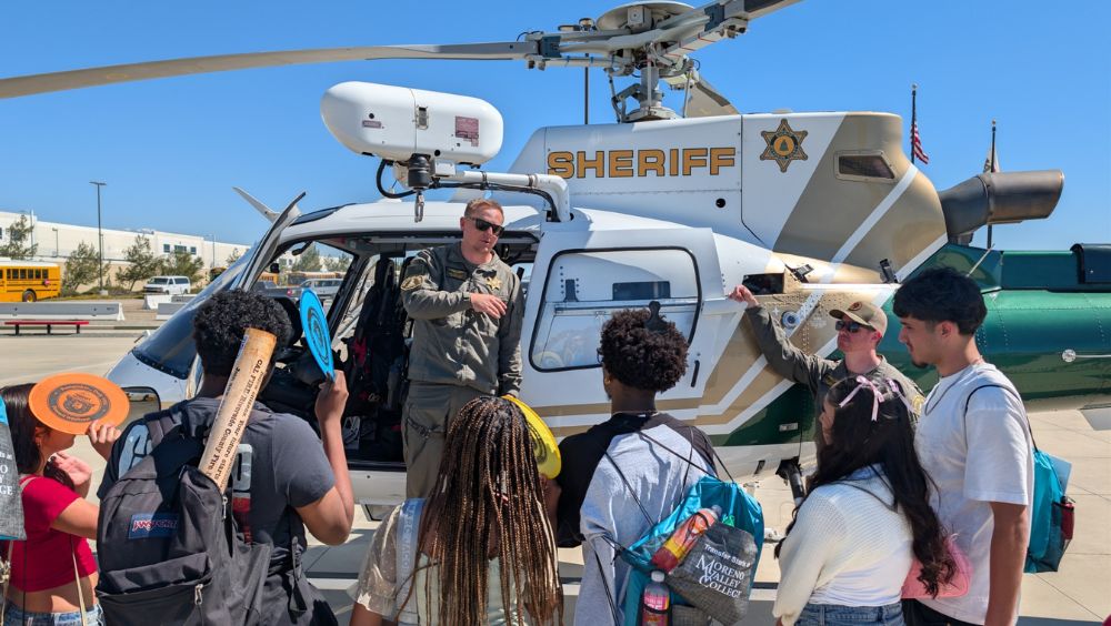 Young high school students listen to a Riverside County Sheriff peace officer next to a department helicopter