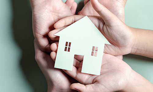 A stack of open palms cradling a house-shaped paper cutout