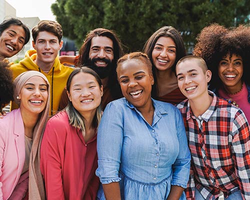 A group of diverse, adult students stand together and smile at the camera